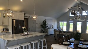 Una cocina amplia con una isla grande, taburetes blancos y modernos apliques colgantes.