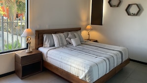 Ein Schlafzimmer mit einem hölzernen Bett, zwei Nachttischen, einem Deckenventilator und einem Fenster mit Blick auf Grünfläche.