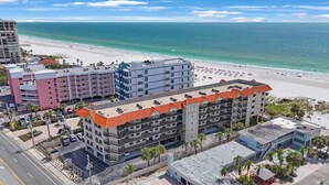 A multi-story hotel with a red-tiled roof, located near a beach with a sandy shore and ocean view.