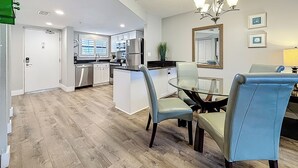 A modern kitchen with stainless steel appliances, a dining area with a glass table and chairs, and a ceiling with recessed lighting.
