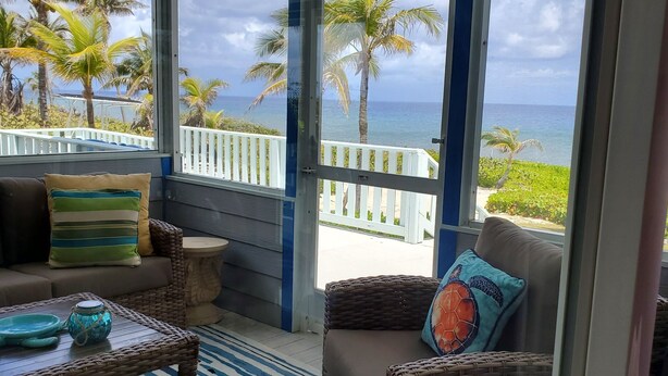 A balcony with wicker furniture, a striped rug, and a view of the ocean and palm trees.