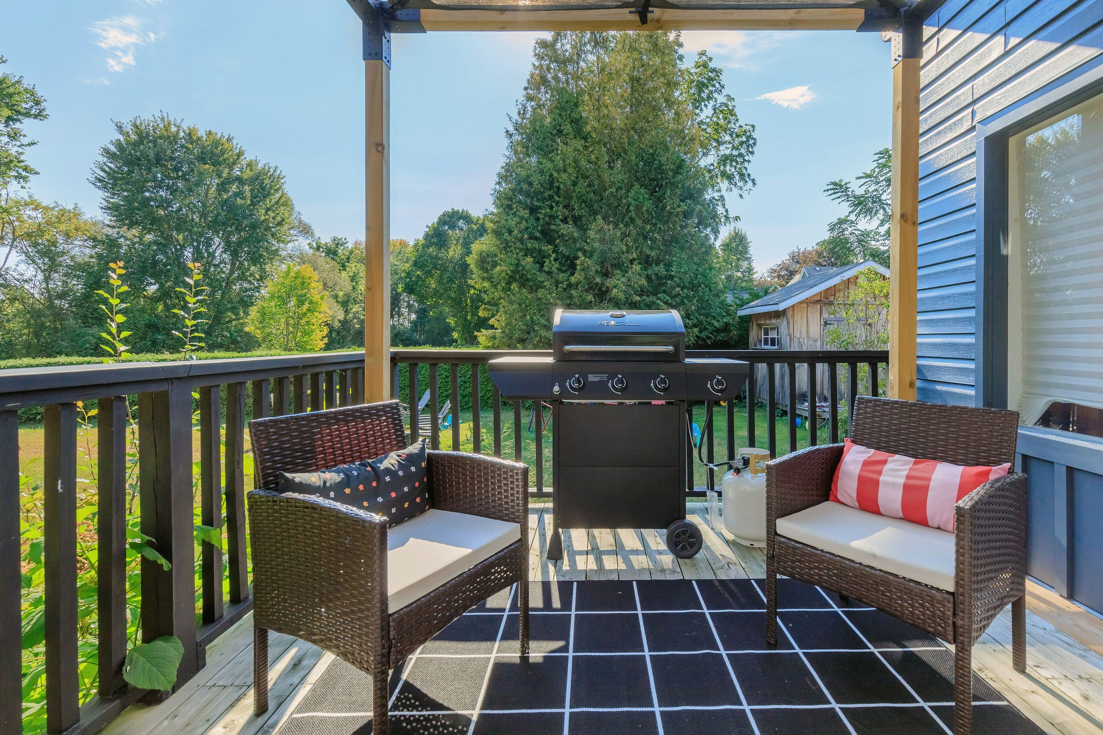 A covered outdoor patio with wicker furniture, a grill, and a view of the surrounding greenery.