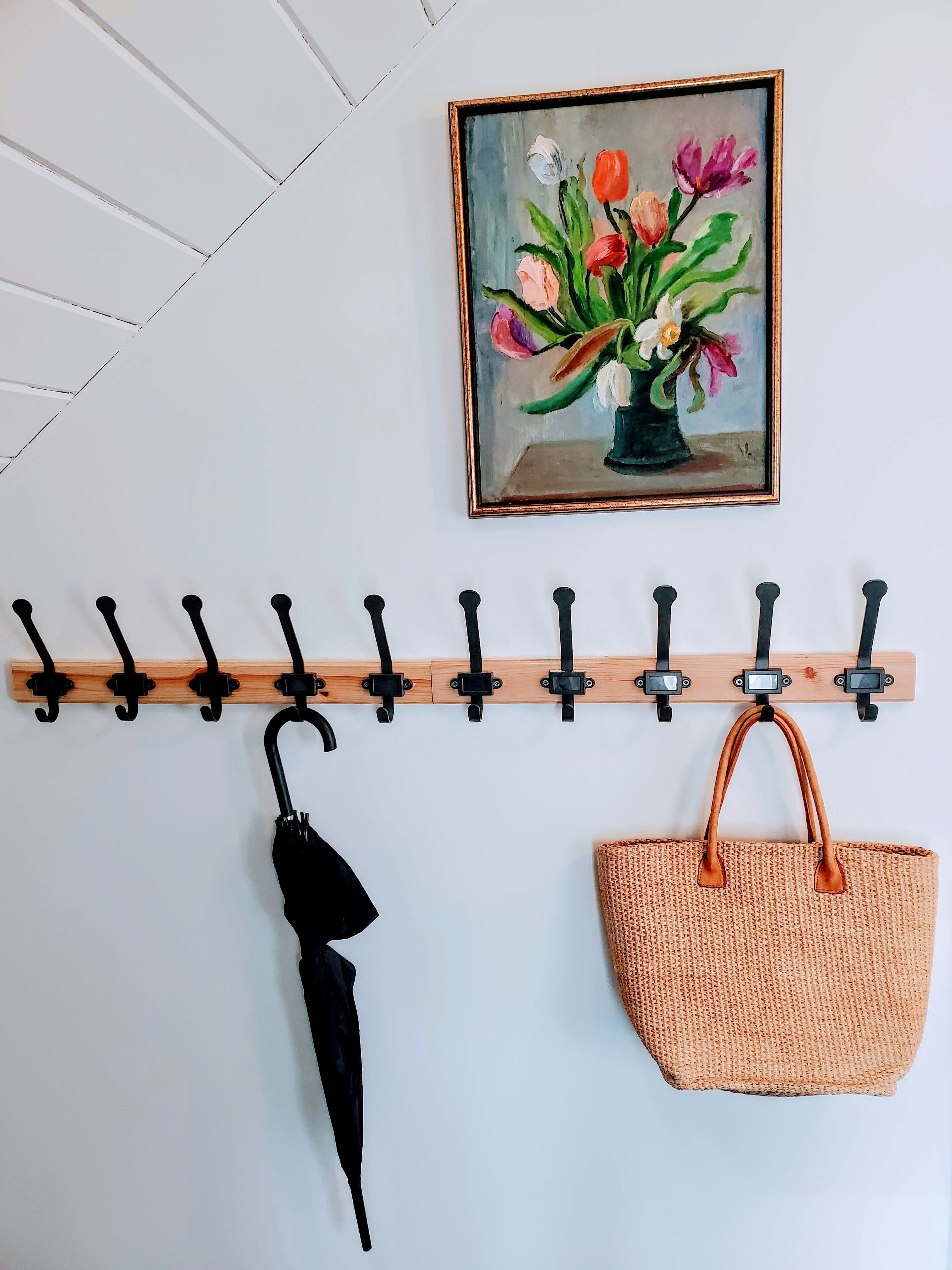A wooden coat rack with hooks, a black umbrella, and a woven handbag.