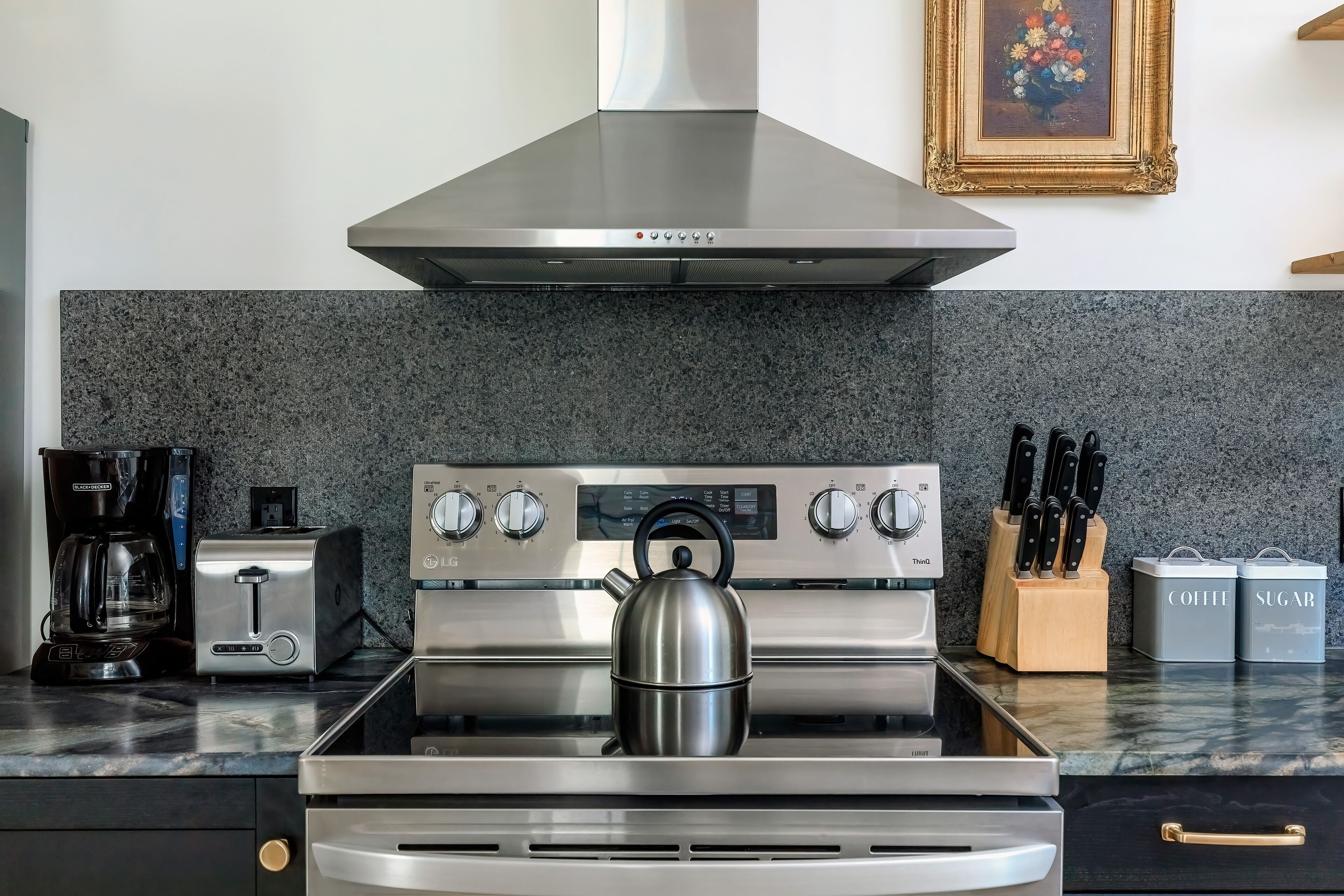 A kitchen with a stainless steel stove, a coffee maker, a toaster, and a kettle.