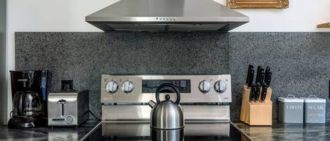 A kitchen with a stainless steel stove, a coffee maker, a toaster, and a kettle.