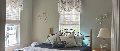 Un dormitorio con cama, mesita de noche, ventilador de techo y decoración de paredes con estrellas de mar.