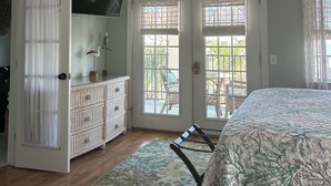 Une chambre à coucher comprenant un lit, un ventilateur de plafond, une commode, un téléviseur et une vue sur l’extérieur par une porte.