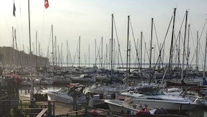 Ein Yachthafen mit zahlreichen vor Anker liegenden Booten, einer hölzernen Anlegestelle und einem Gebäude auf der linken Seite.