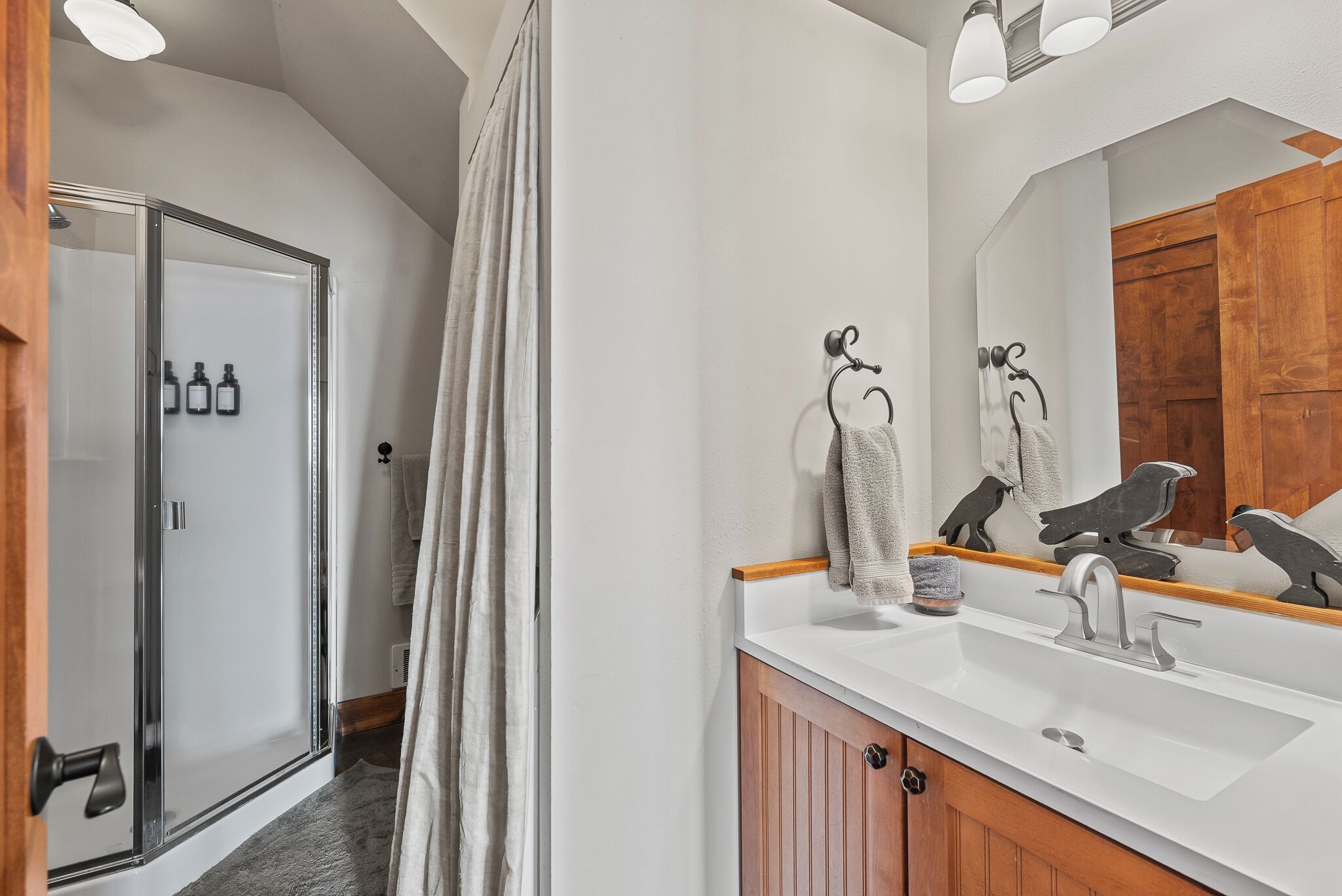 Un baño con ducha, lavabo, espejo y un mueble de madera.
