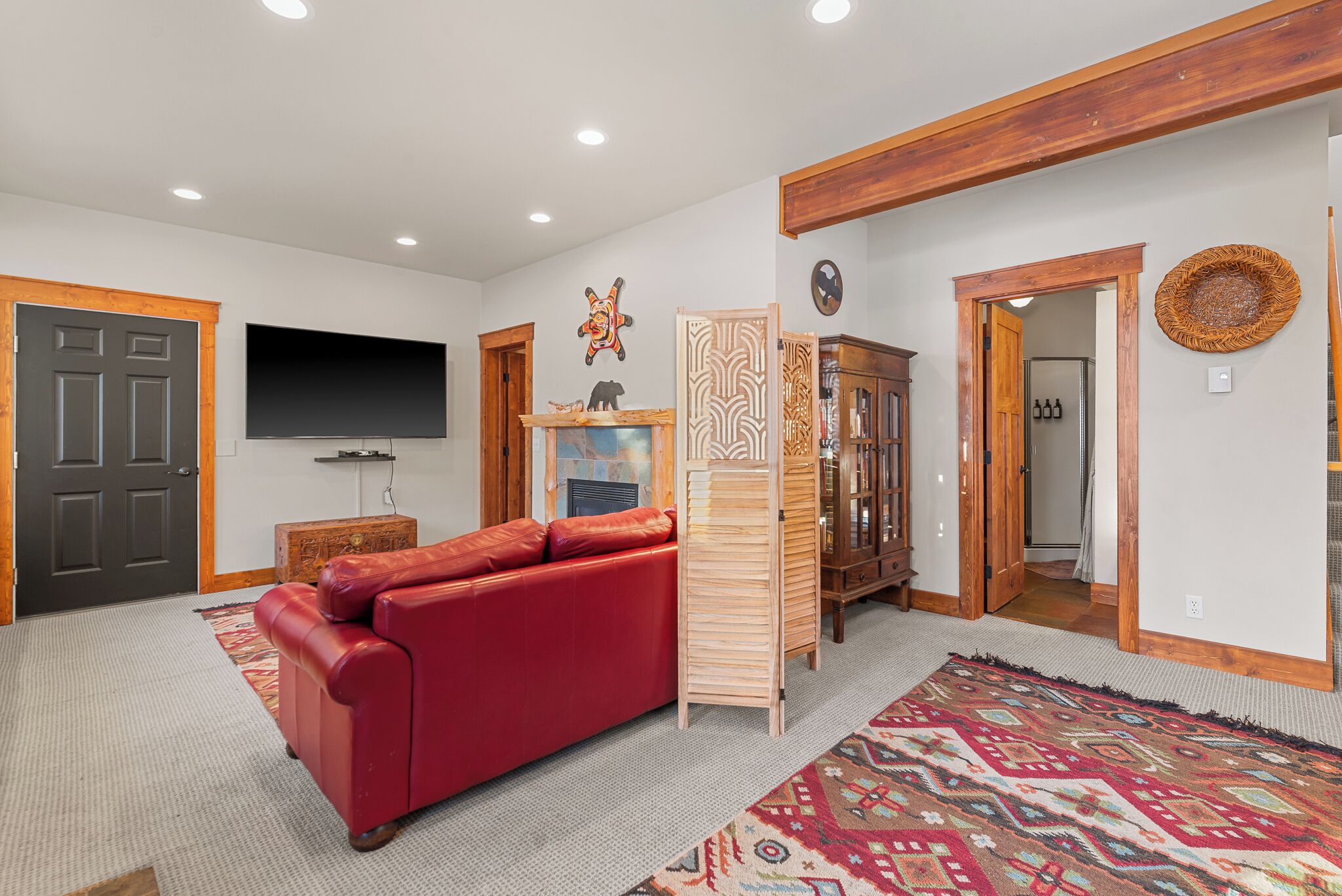 Un salon avec un canapé rouge, un téléviseur à écran plat, un meuble en bois et un tapis à motifs.