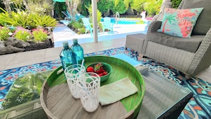 A patio area with a wicker sofa, a green tray with a bowl of strawberries, and two blue water bottles.
