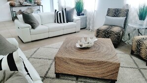 A living room with a white sofa, a woven ottoman, and a zebra-patterned chair.