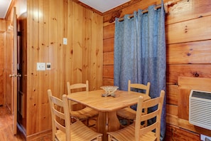 A wooden interior with a dining table and chairs, a blue curtain, and a wall-mounted air conditioning unit.