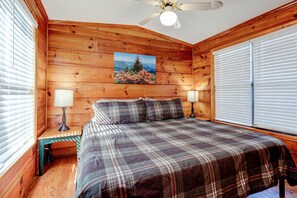 A wooden-paneled bedroom with a bed, two bedside lamps, and a ceiling fan.