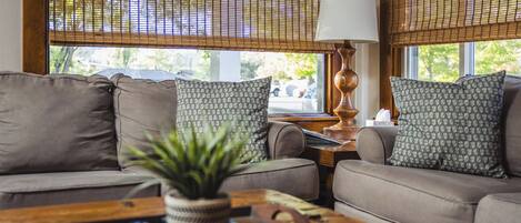 A living room with a sofa, two patterned pillows, a lamp, and a plant on a wooden coffee table.