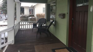 A porch with a wooden floor, a chair, a door, and a mailbox.