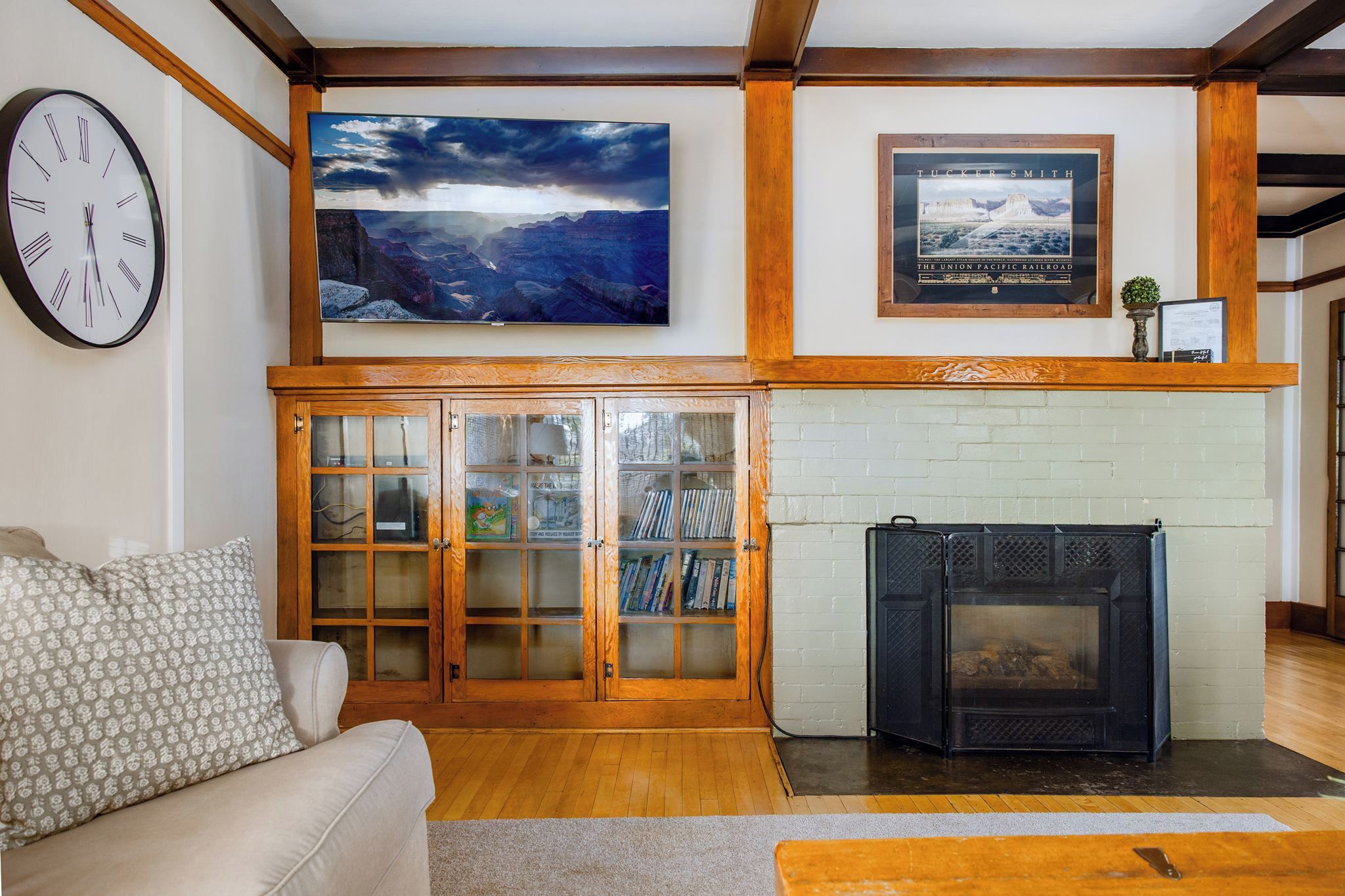 A living room with a fireplace, a large painting, a clock, and a bookshelf.