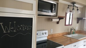 A kitchen with a blackboard displaying "Welcome", a microwave, a stove, a sink, and wooden cabinets.
