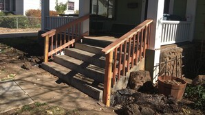 A house with a wooden staircase leading to a porch, a stone stump, and a wooden planter.