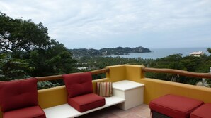 Eine Terrasse mit gelber Geländer, roter und weißer Möbel und Blick auf das Meer und die Hügel.