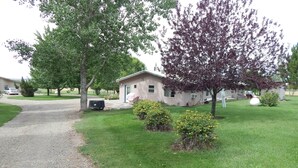 Il s’agit d’une propriété résidentielle dotée d’une allée en gravier, d’une petite maison et d’une pelouse agrémentée d’arbustes et d’arbres.