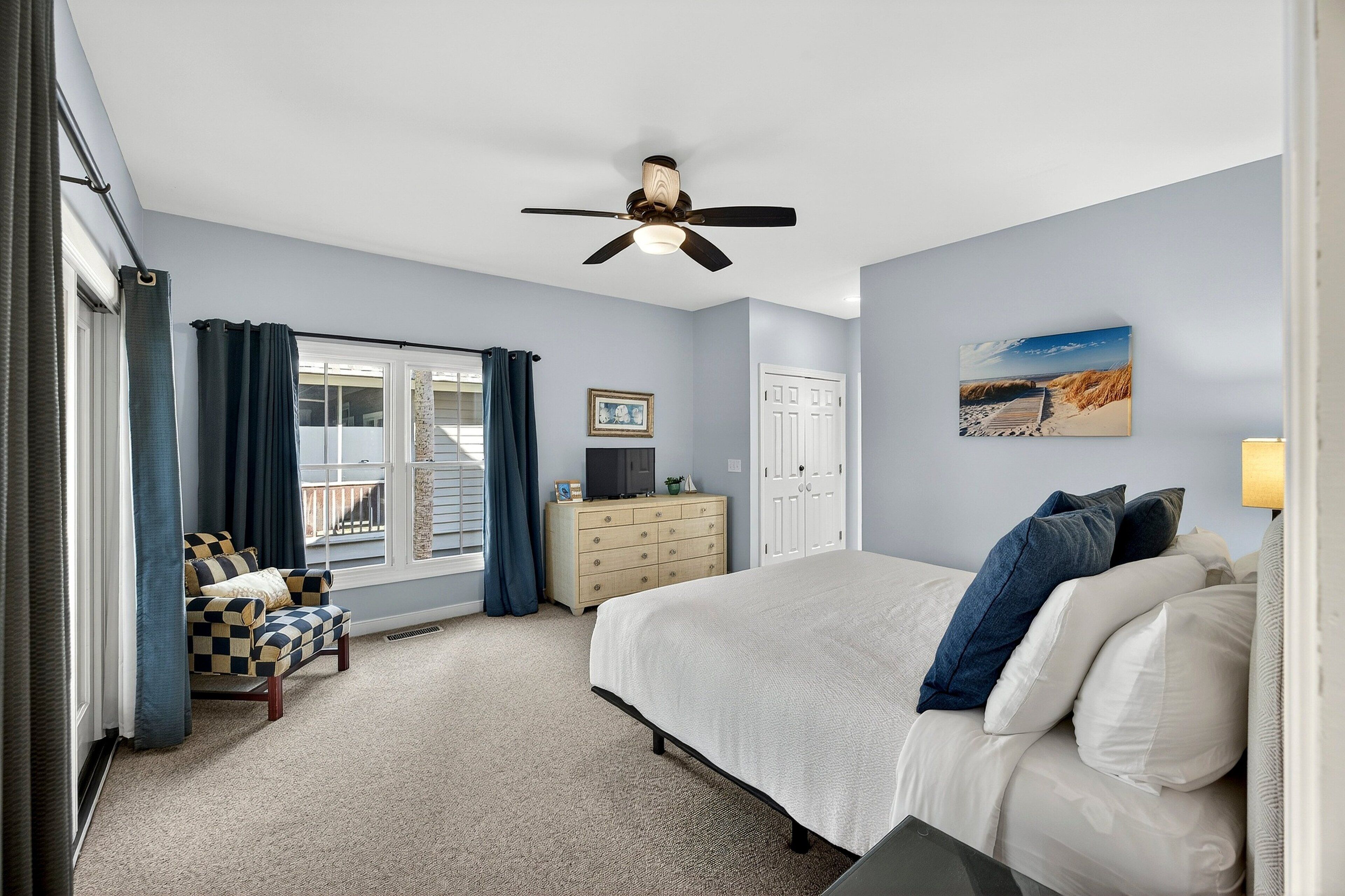 A bedroom with a bed, a dresser, a chair, a ceiling fan, and a window with curtains.