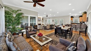 A spacious living area with a high ceiling fan, a dining table with chairs, and a large window providing natural light.