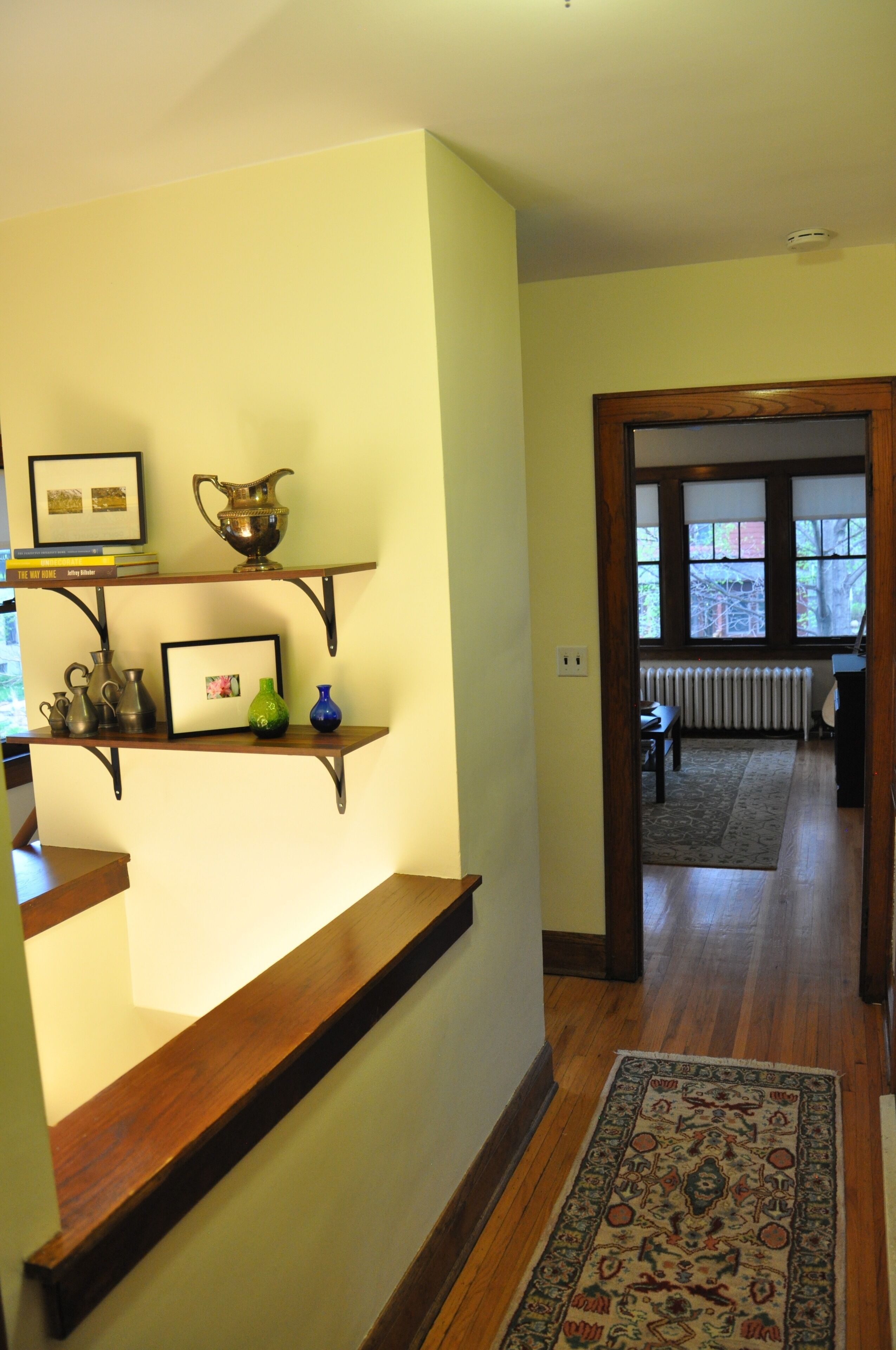 A hallway with wooden flooring, a patterned rug, and a shelf with decorative items.