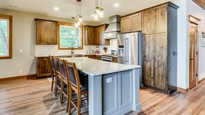 A modern kitchen with a large island, wooden cabinets, stainless steel appliances, and pendant lighting.