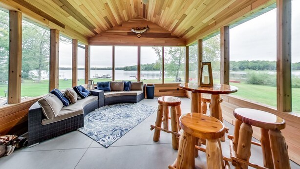 A spacious wooden room with a large window, a ceiling fan, a sofa with cushions, and a small wooden table.