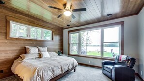 A bedroom with a large bed, a ceiling fan, and a view of a golf course through a large window.