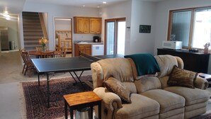 A living room with a sofa, a coffee table, and a ping pong table. There is a kitchen in the background with wooden cabinets and a sink. - Spacious Quiet Country Home With Stunning Views from Private Patio (Inkom)