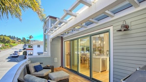 A covered patio with outdoor seating, a sliding glass door leading to a kitchen, and a street view in the background. - Sunsetter in Avila Beach - 2 min walk to beach, located in Ocean 17 (Avila Beach)