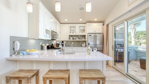 A modern kitchen with a large island, white cabinetry, and a sliding glass door leading to an outdoor area. - Sunsetter in Avila Beach - 2 min walk to beach, located in Ocean 17 (Avila Beach)