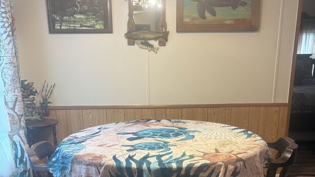 Un coin repas avec une table ronde recouverte d’une nappe à motifs, entourée de chaises en bois.