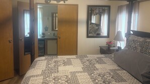 Een slaapkamer met een bed, een houten hoofdbord, een nachtkastje, een lamp, een spiegel en een deur naar een badkamer.
