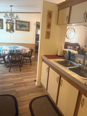 Een keuken met houten kastjes, een spoelbak en een eethoek met een tafel en stoelen.