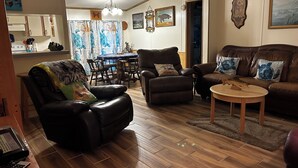 Een woonkamer met een leren bank, een fauteuil, een salontafel en een eethoek met een tafel en stoelen.