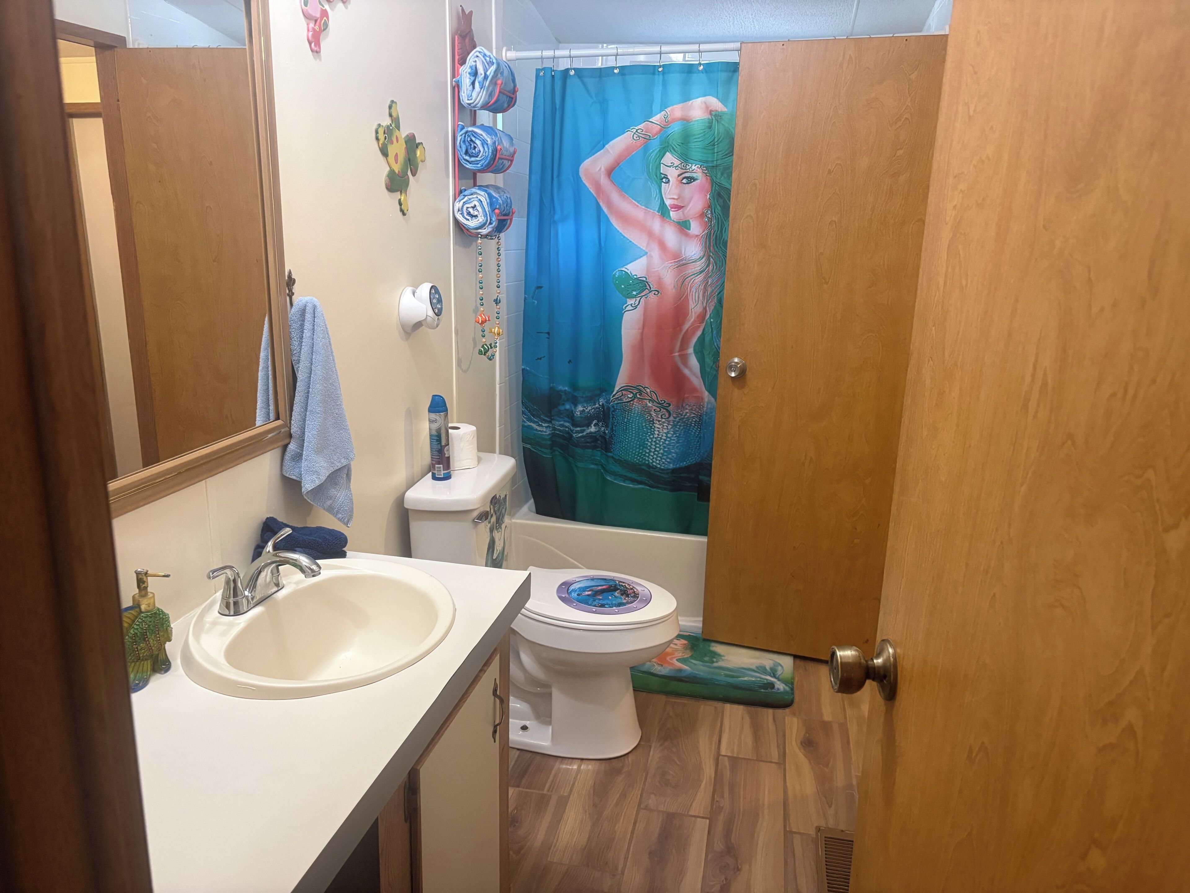 A bathroom with a sink, toilet, shower curtain, and decorative items.