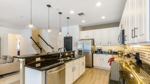 A modern kitchen with white cabinets, a black granite countertop, stainless steel appliances, and pendant lighting.