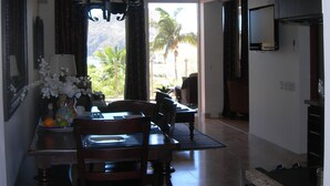 A dining area with a table, chairs, and a chandelier. There is a view of palm trees through the window.