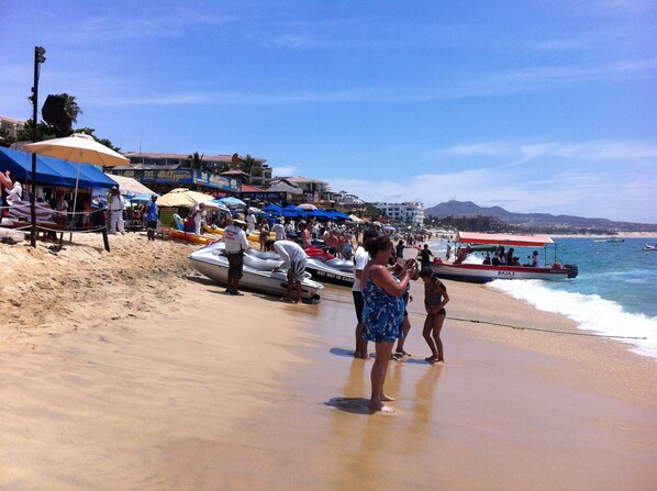 Una playa con gente, barcos y sombrillas.