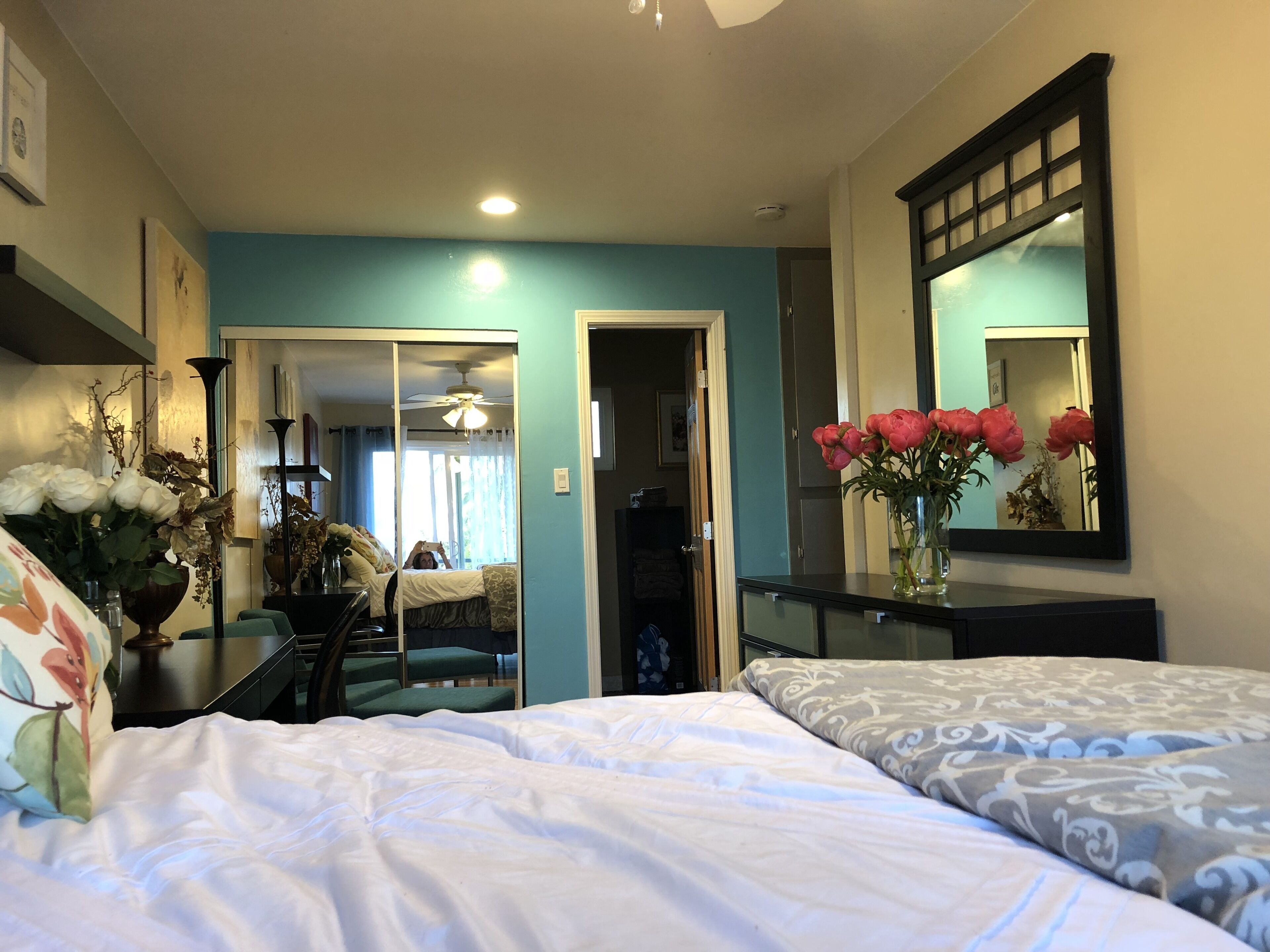 A hotel room with two beds, a mirror, a vase with flowers, and a ceiling fan.