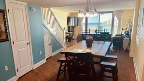 A dining area with a wooden table, chairs, and a vase centerpiece. A staircase leads to an upper level. - 2bd2 1/2ba sleeps8 1st&2fltownhouse onbeachw/dolphin views,boating,tennis,fishin (Pensacola)