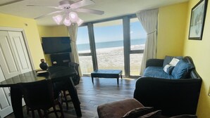 A living room with a view of the beach, a ceiling fan, a TV, and a dining area with chairs and a table. - 2bd2 1/2ba sleeps8 1st&2fltownhouse onbeachw/dolphin views,boating,tennis,fishin (Pensacola)
