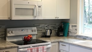 A kitchen with white cabinets, a microwave, an oven, and a window with a view of trees. - NEW! Tranquil Oceanfront Gem with Hot-tub 3 BDRM + Den, 3 BATH (Waldport)