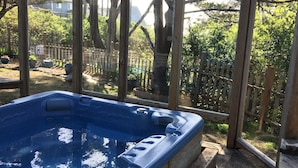 A hot tub in a covered outdoor area with a wooden deck and a view of a fenced yard with trees and a house in the background. - NEW! Tranquil Oceanfront Gem with Hot-tub 3 BDRM + Den, 3 BATH (Waldport)