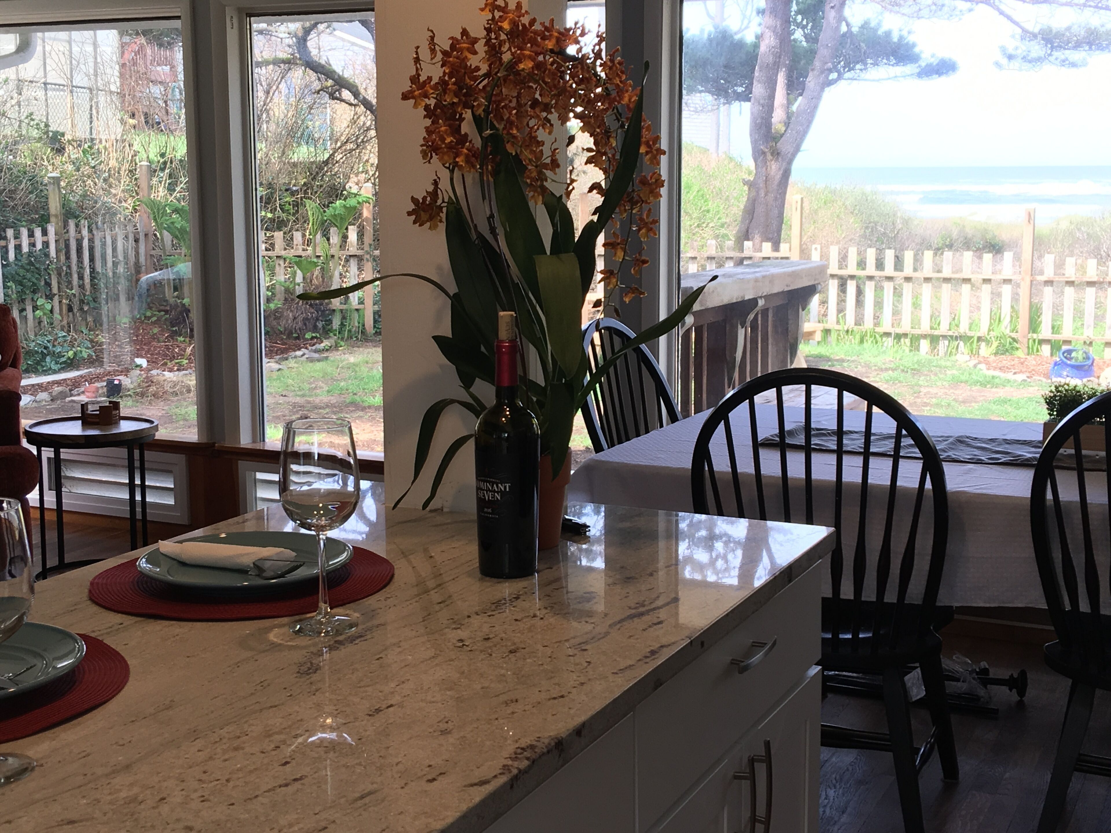 Una zona de comedor con encimera de mármol, una copa de vino, una botella de vino y una planta en maceta con flores anaranjadas.