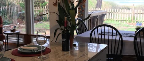 Una zona de comedor con encimera de mármol, una copa de vino, una botella de vino y una planta en maceta con flores anaranjadas.