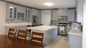 A modern kitchen with grey cabinets, a stainless steel refrigerator, a built-in oven, and a large island with bar stools. - * Living Large * Newly Built * Disneyland & Beaches (Midway City)